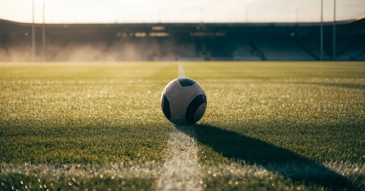 Uma bola de futebol no ponto central de um relvado, à luz da manhã